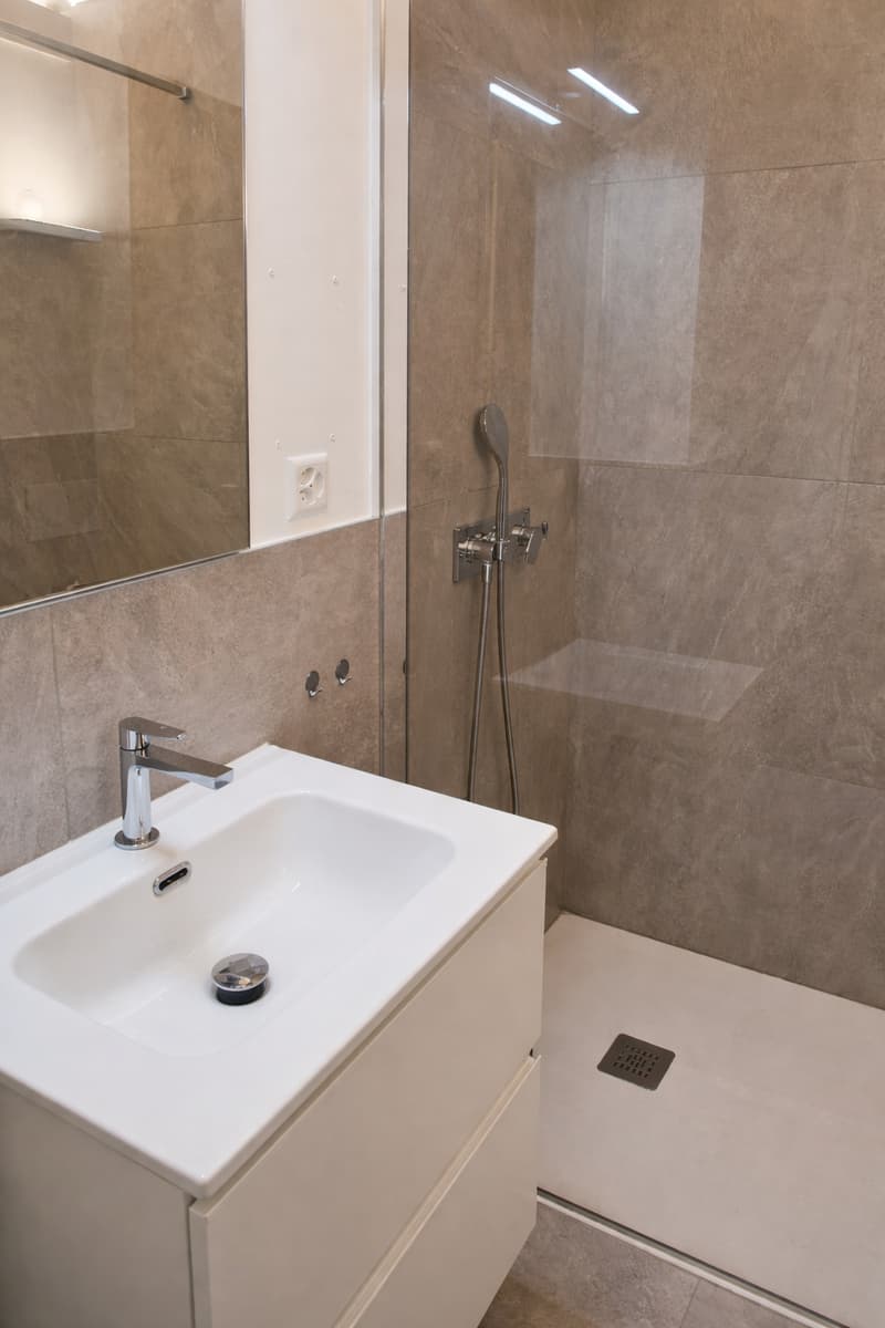 Bathroom: White tile, mirror, shower enclosure, sink, faucet, shower head, and drainage