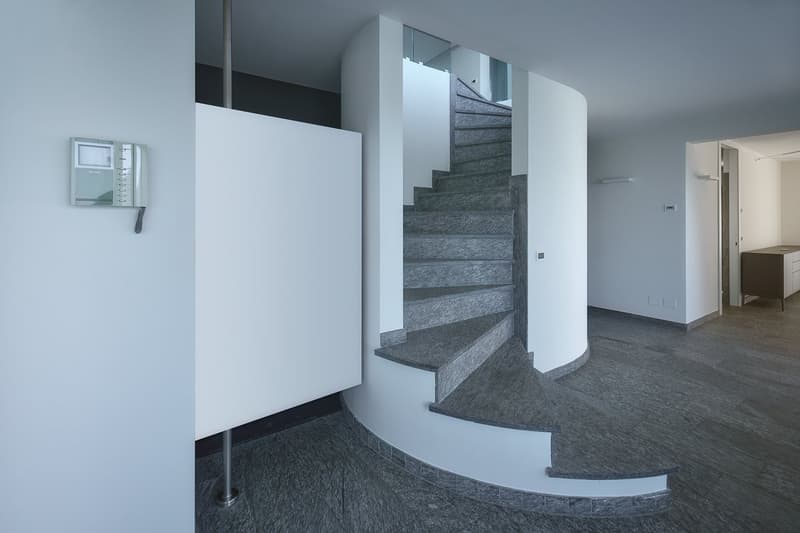 Entrance hall, spiral staircase, white walls, gray flooring, glass elements, telephone mounted on the wall, cabinet in the hallway