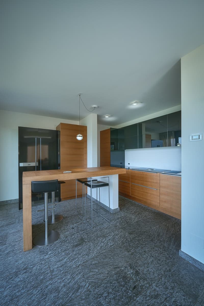 large island countertop with stools, modern open-plan kitchen, wooden cabinets, stainless steel appliances, white walls, gray floors