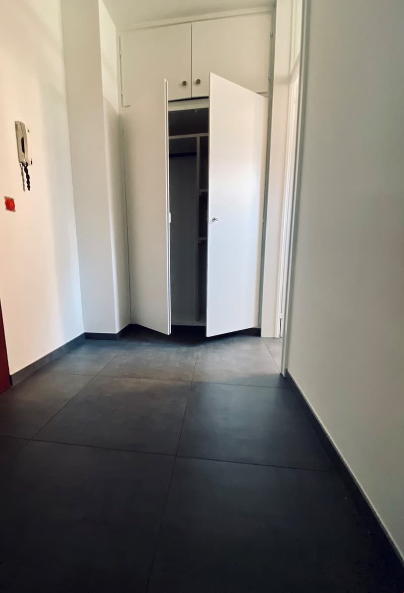 Empty room with white walls, black floor, open closet, and a telephone on the wall