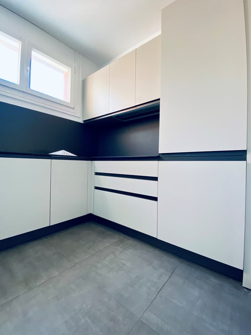 modern kitchen with white cabinets, black countertops, gray floor, windows, extractor hood