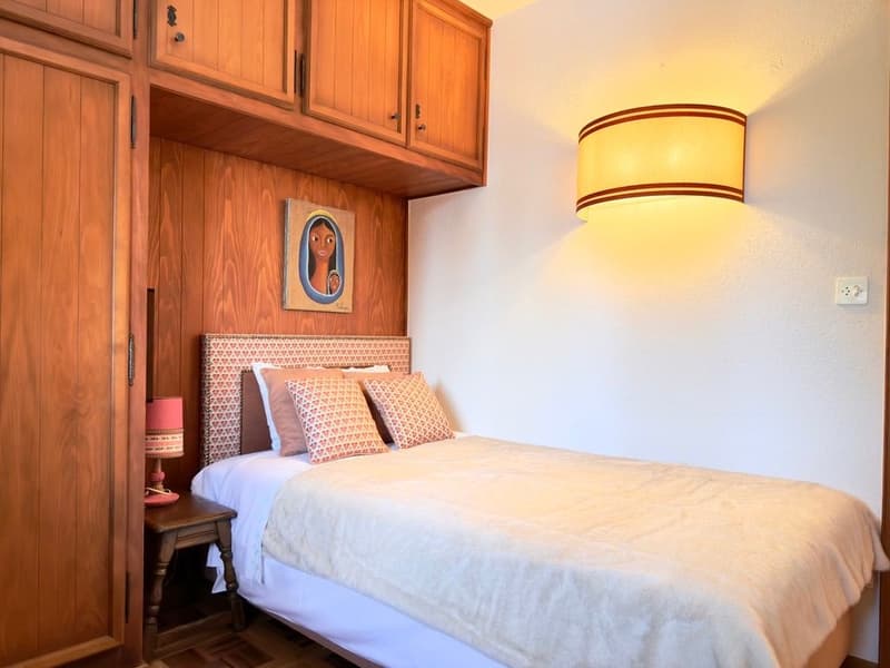 Bedroom with a bed, nightstand, wooden cabinets, wall lamp, and a picture frame