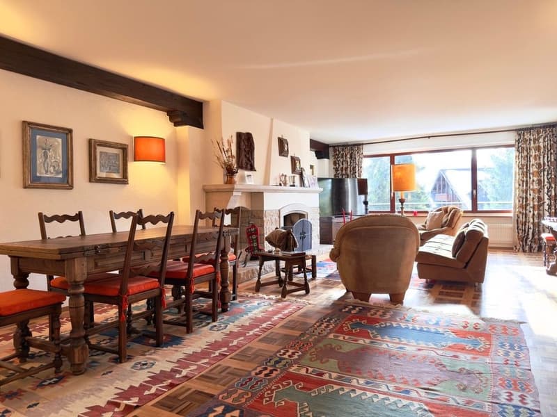 Dining room with wooden table, chairs, fireplace, rugs, lamps, couch, and window with curtains