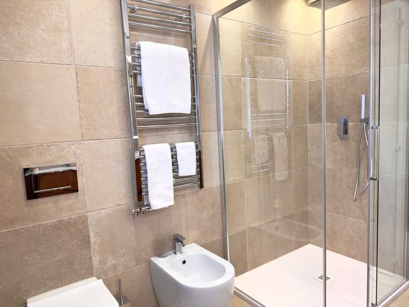 modern bathroom with walk-in shower, bidet, toilet, towel rack, tiled walls