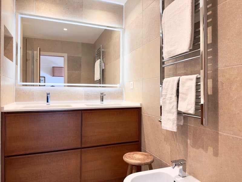 modern bathroom with large mirror, wooden cabinet, double sink, wooden stool, towel rack, and bathtub