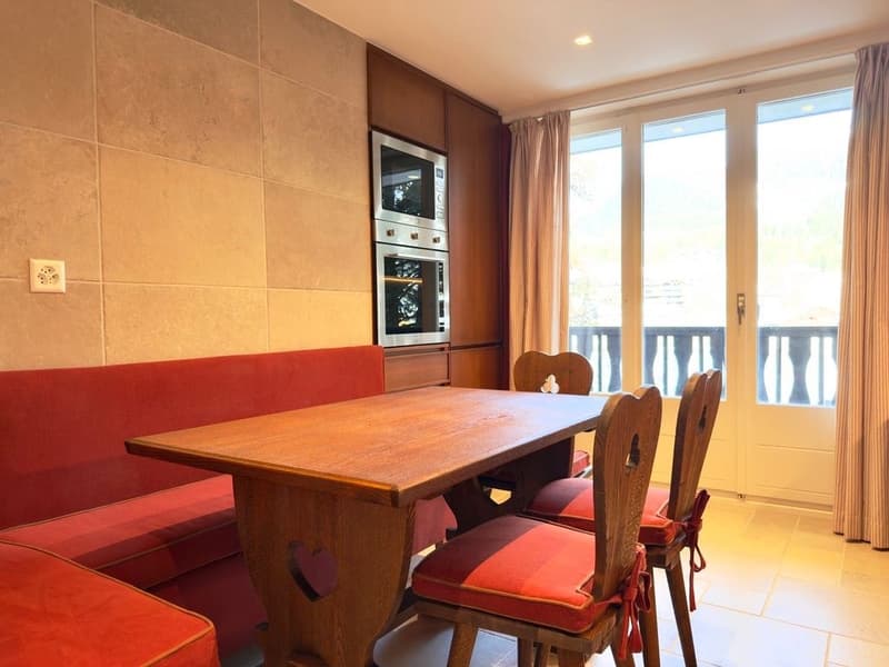 Dining area with wooden table, red cushioned chairs, red cushioned bench, double oven, balcony with view
