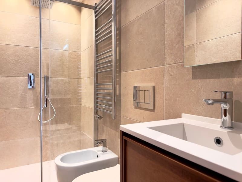 modern bathroom with glass shower, white sink, wooden cabinet, beige tiles, bidet, towel rack