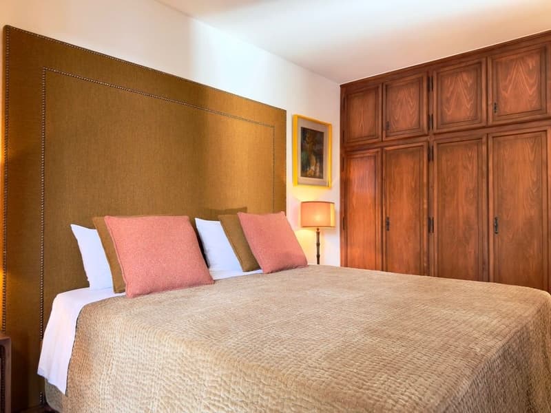 A bedroom with a bed, pillows, a lamp, a picture frame, and wooden cabinets
