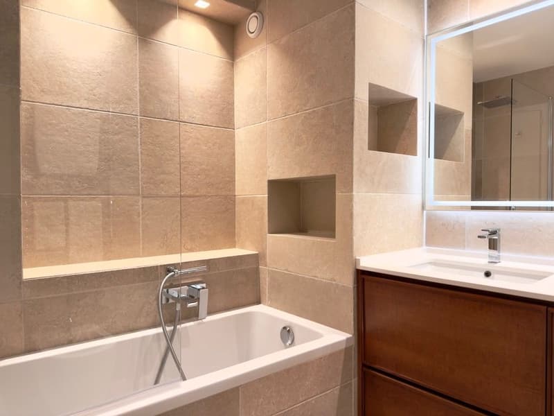 Bathroom with bathtub, sink, mirror, wooden cabinet, tiled walls, shower area