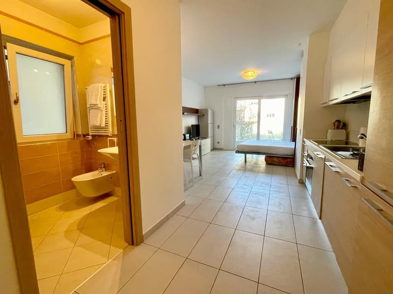 A small room, with a sink, small bathroom, a chair, and a small bed
