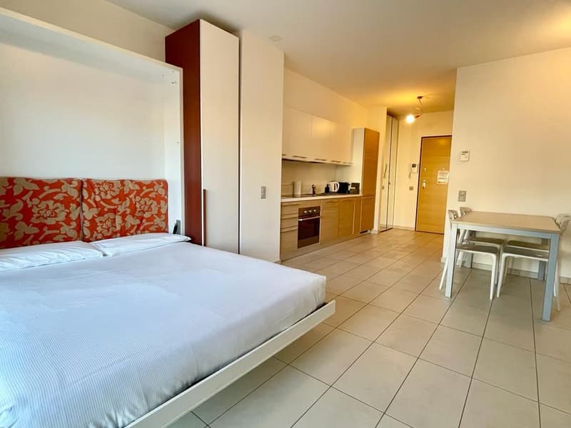 A simple bedroom with a bed, pillows, and a dining table with chairs.