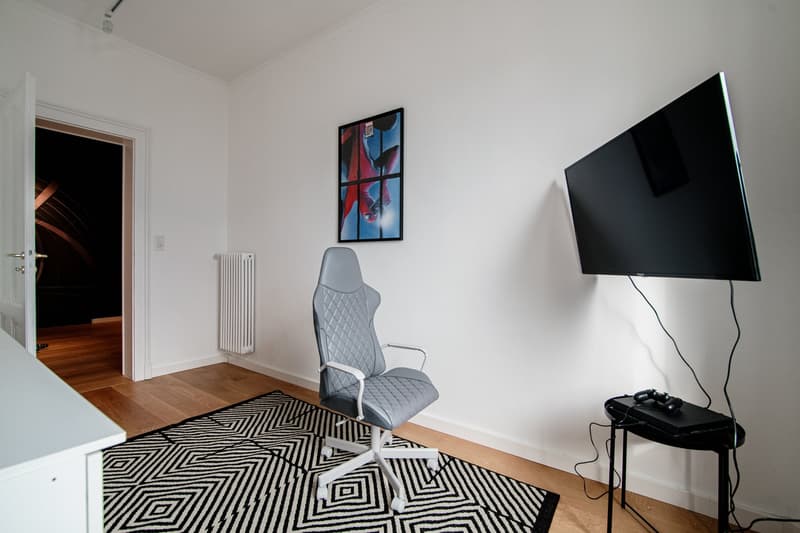 black and white rug, office chair, flatscreen TV on the wall, game console, radiator