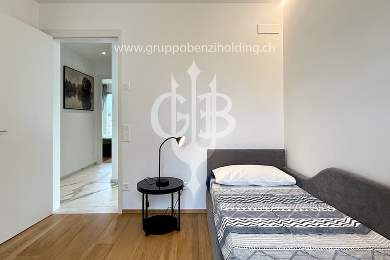 A single bed with white pillow in a room with a wall lamp and wooden floor