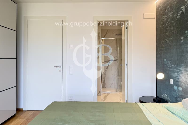 modern styled bedroom, green bed, white doors, marble bathroom with glass shower door, nightstand with lamp, wooden floor