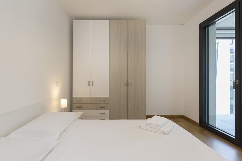 wooden floor, white walls, double bed, lamps, large wardrobe, drawers, glass door to balcony