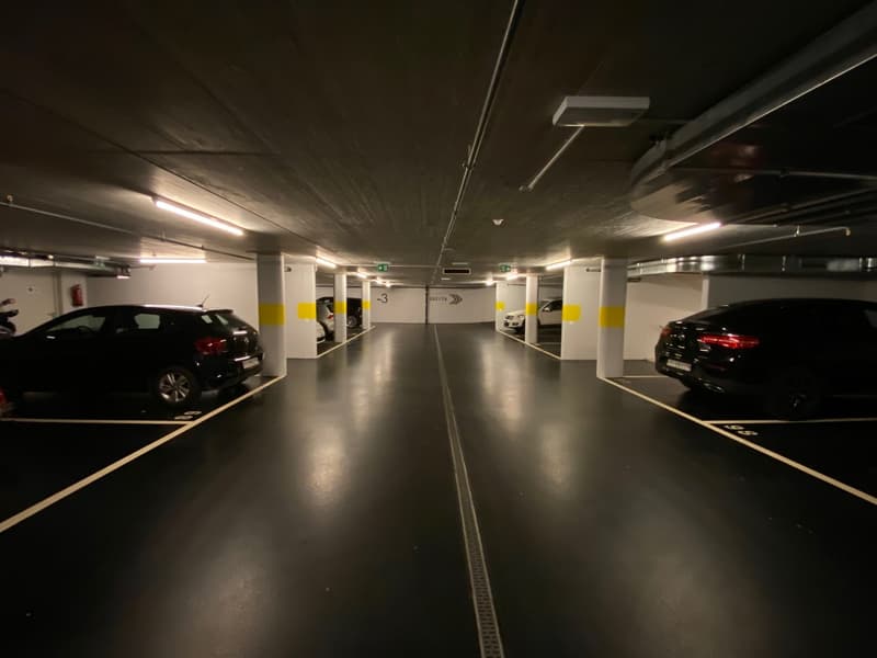 underground parking lot with a few parked cars, white walls, yellow and white markings, and fluorescent lights