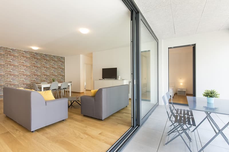 large windows, balcony, grey sofas, wooden floors, coffee table, TV, dining table, chairs