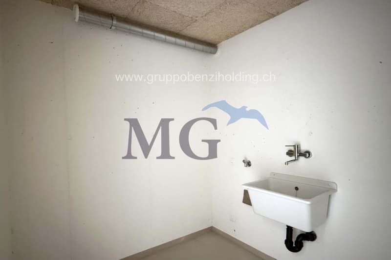 Small, unfurnished room with white walls, single sink, and logo on the wall