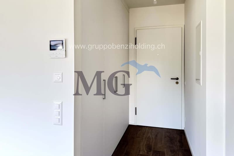 White walls, wooden floor, entrance door, electrical switch, surveillance camera