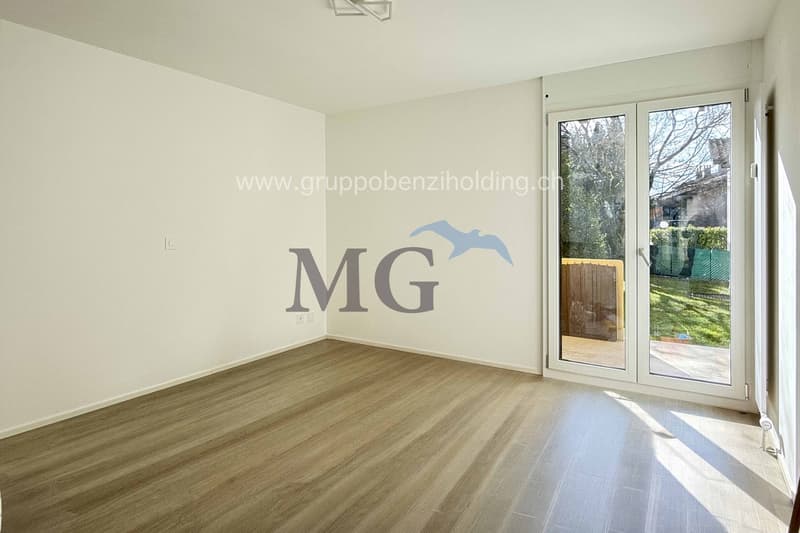 Empty room with white walls, wooden floor, sliding glass door leading to a garden, wooden gate