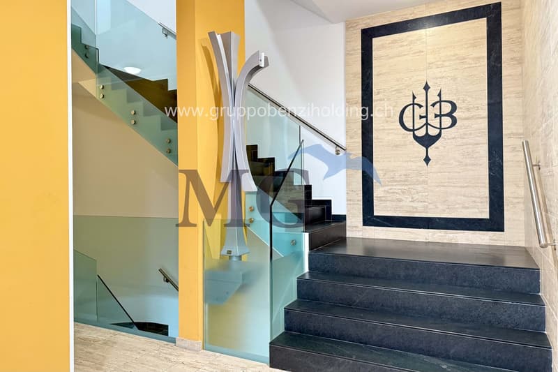 Glass staircase with a black marble handrail, logo on the wall