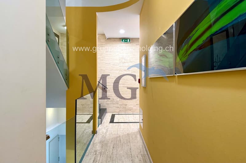Tiled hallway, glass railings, yellow walls, art pieces, emergency exit sign