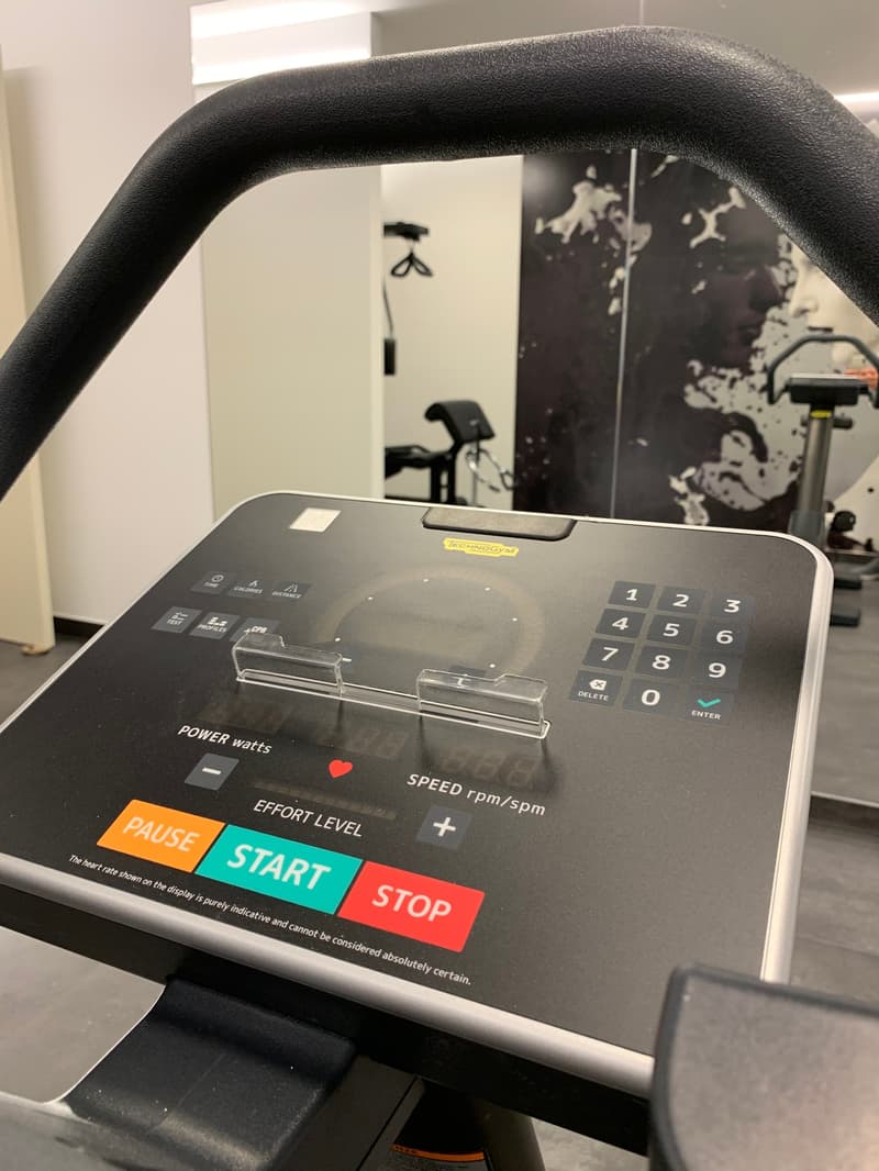 The image shows a piece of exercise equipment, likely a treadmill or elliptical machine. The control panel displays various metrics such as power, speed, and effort level, as well as buttons to start, pause, and stop the machine.