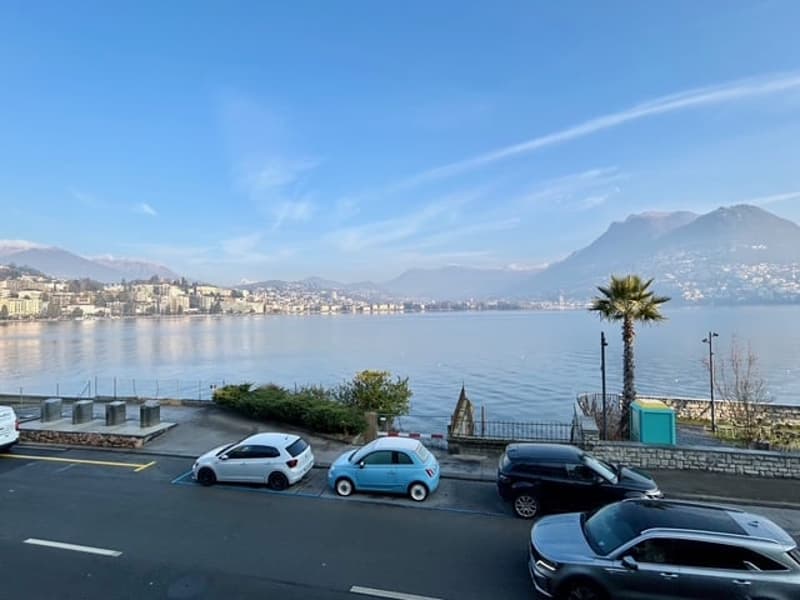 A view of a lakeside road with a view of the water and mountains.