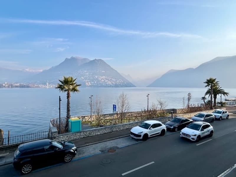 A scenic view with multiple cars parked alongside the road with mountains and a lake in the distance