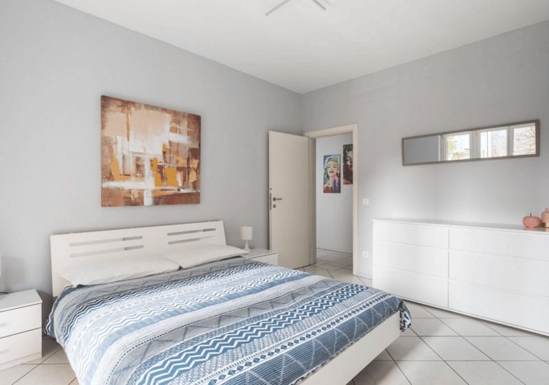 bed, nightstand, lamp, artwork, white cabinets, mirrored wall, doorway