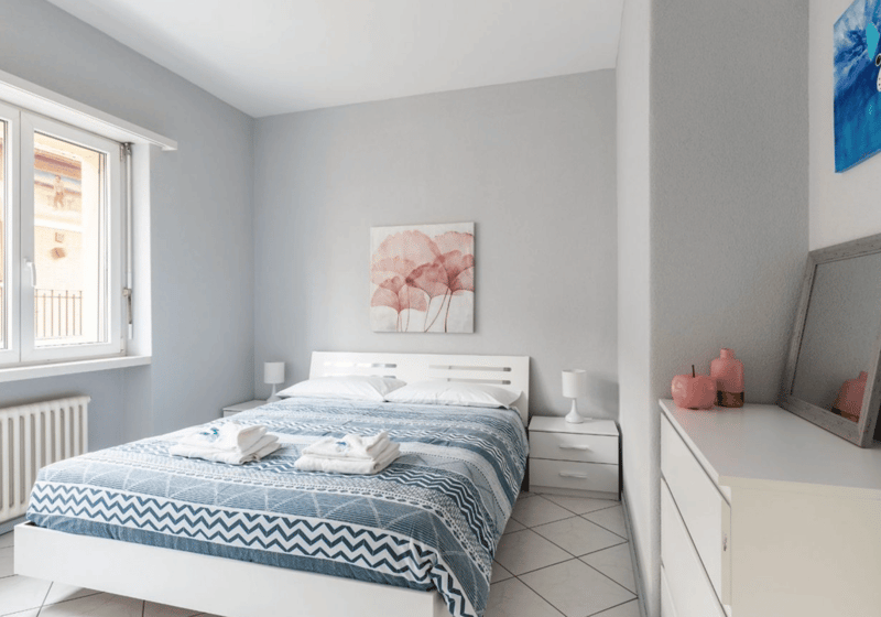 double bed with white sheets, grey walls, white tiled floor, large window with balcony access