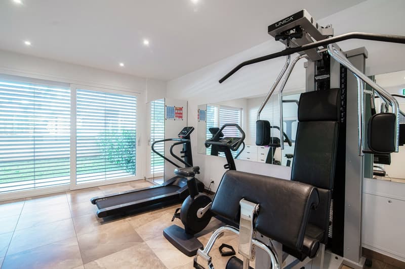 A room with exercise equipments, a treadmill, a weight training machine, a lat pulldown machine, mirrors, and lights