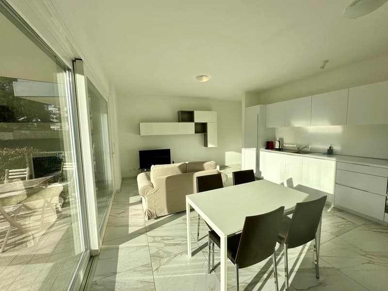 Open plan living and dining area, modern furniture, white tile flooring, double doors leading to balcony, large windows, TV, couch