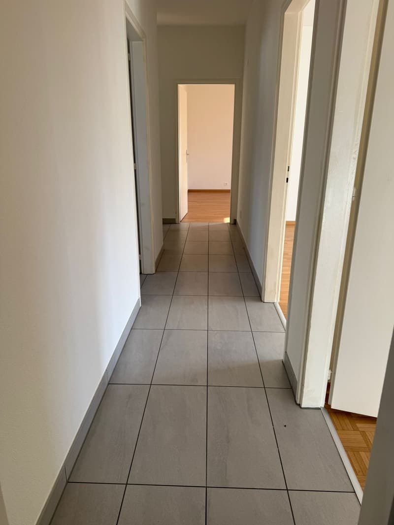 Corridor, white walls, tile flooring, doors leading to rooms, open doorway at end