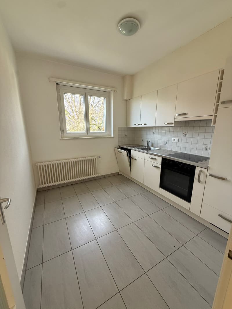 Modern kitchen with white cabinetry, tiled flooring, under window radiator, stainless steel oven and sink