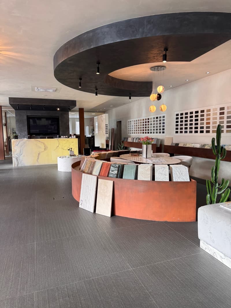 large, open room, gray flooring, yellow marble counter, round display of tiles, hanging lights, wall with color tiles