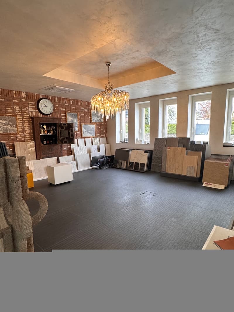 ample space with brick walls, chandelier, windows, clock, display of tiles and wooden flooring