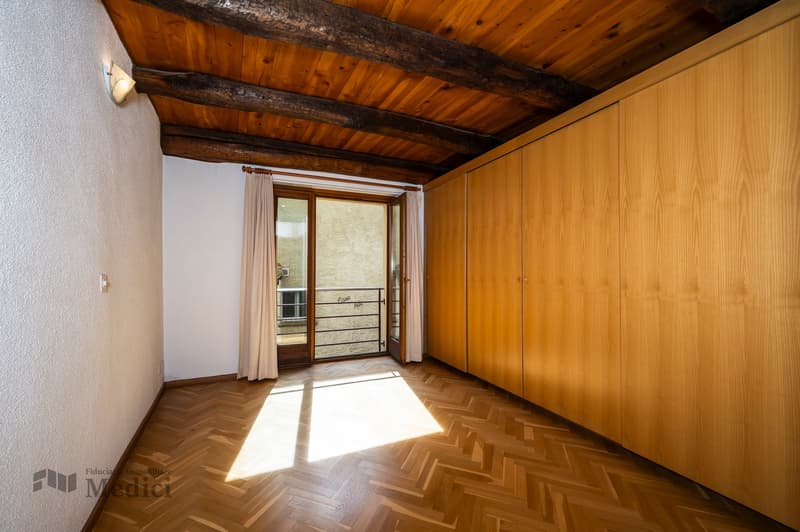 large room with wooden floor, wooden wall cabinets, wooden beams ceiling, glass door to balcony