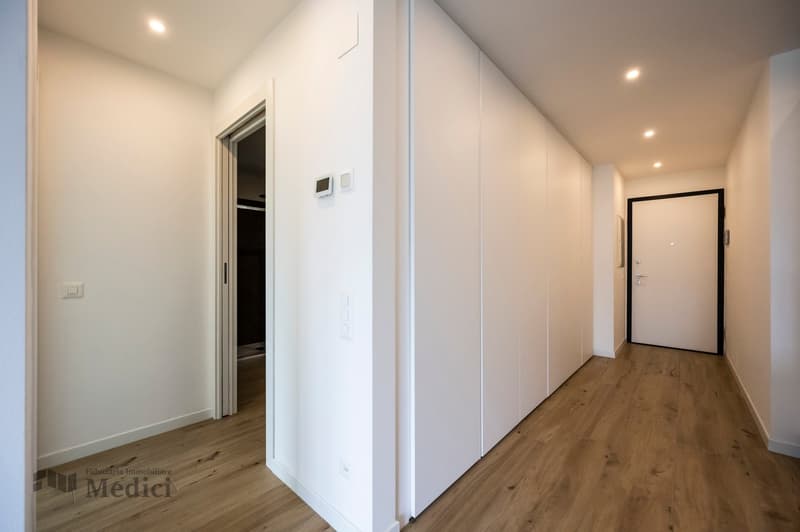Wooden floor, white walls, hallway, white door, two closed doors, one open door to a dark room
