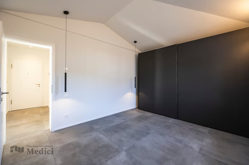 Large room with white walls, tiled floor, large black sliding closets, entrance door, wall switches, pendant lighting.