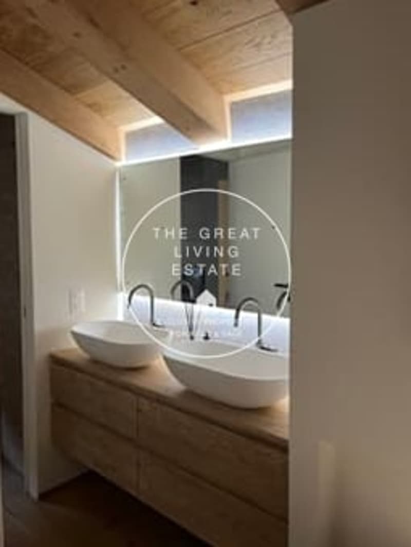 Wooden ceiling beams, vanity with double sinks, large mirror with illuminated text 'The Great Living Estate'