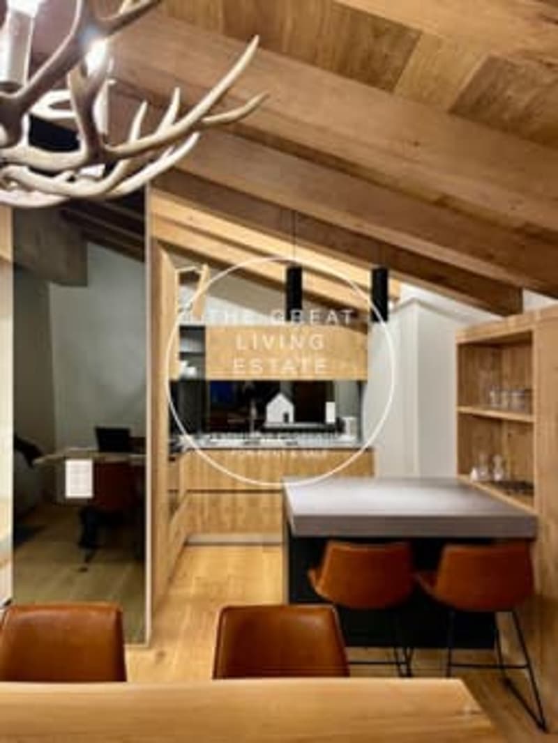 Rustic living room with wooden ceiling beams, a large antler chandelier, a fireplace, and leather armchairs around a wooden coffee table