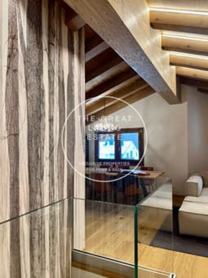 The image shows the interior of a building with wooden beams and walls, and a glass door or window that appears to lead to a balcony or terrace area.