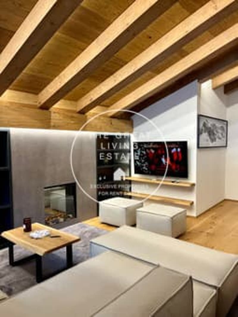 Open-concept living room with exposed wooden beams on the ceiling, a fireplace, a large sofa, and a coffee table.