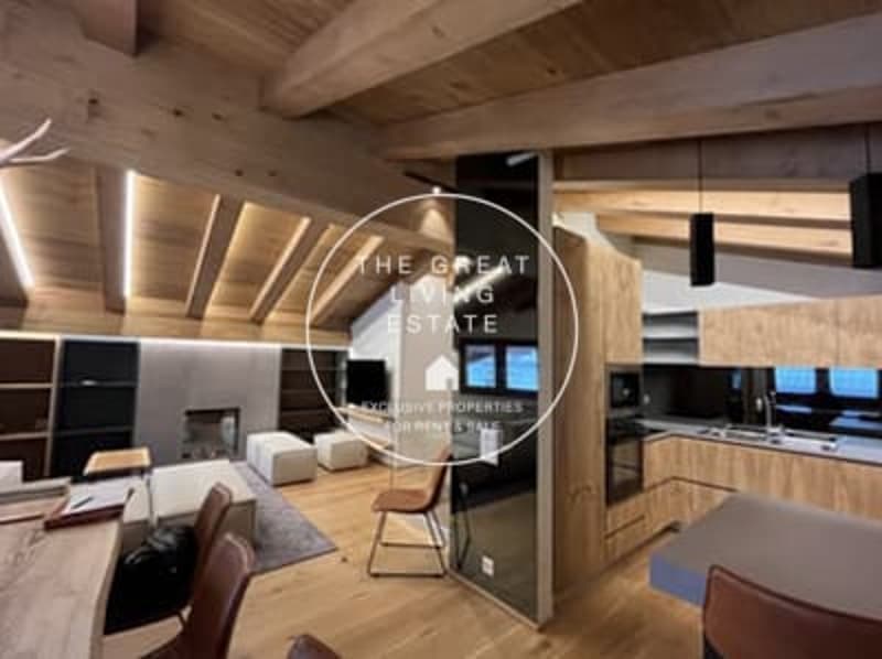 Open-concept living room with wooden beams and ceiling, modern kitchen with wooden cabinets, large windows providing natural light, and a fireplace visible.