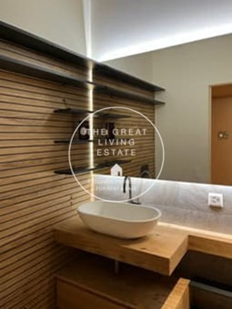 Wooden vanity with a vessel sink, modern faucet, and a framed mirror with the text 'The Great Living Estate' on the wall.