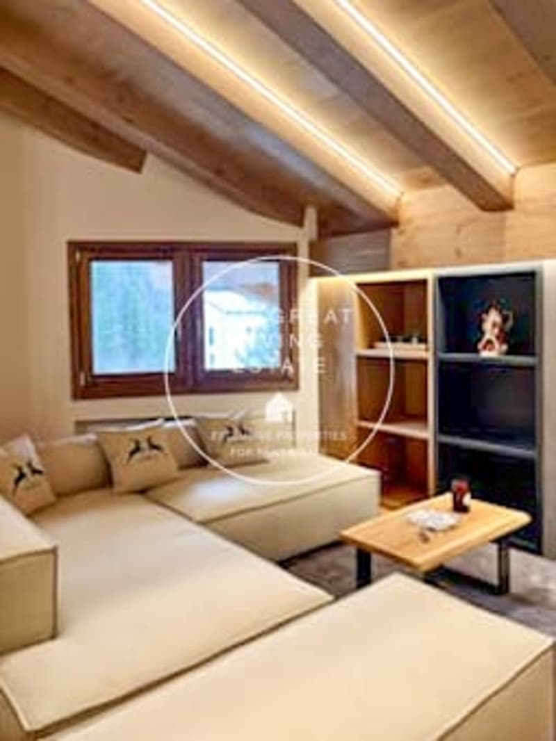 Cozy living room with wooden beamed ceiling, large windows, comfortable sofas, and a fireplace.