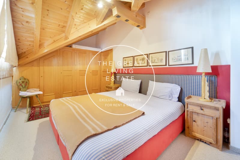 Cozy bedroom with wooden beams and paneling, red accent wall, striped bedding, wooden nightstands, and framed artwork on the walls.