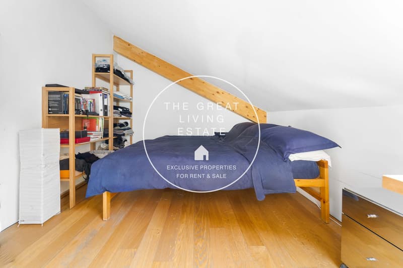 slanted ceiling, wooden bed, two blue pillows, wooden shelf with books and clothes, white folding screen