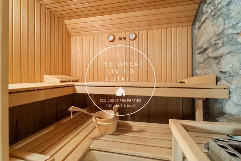 A wooden sauna room with three benches, wooden buckets, a ladle, and wall-mounted clocks.